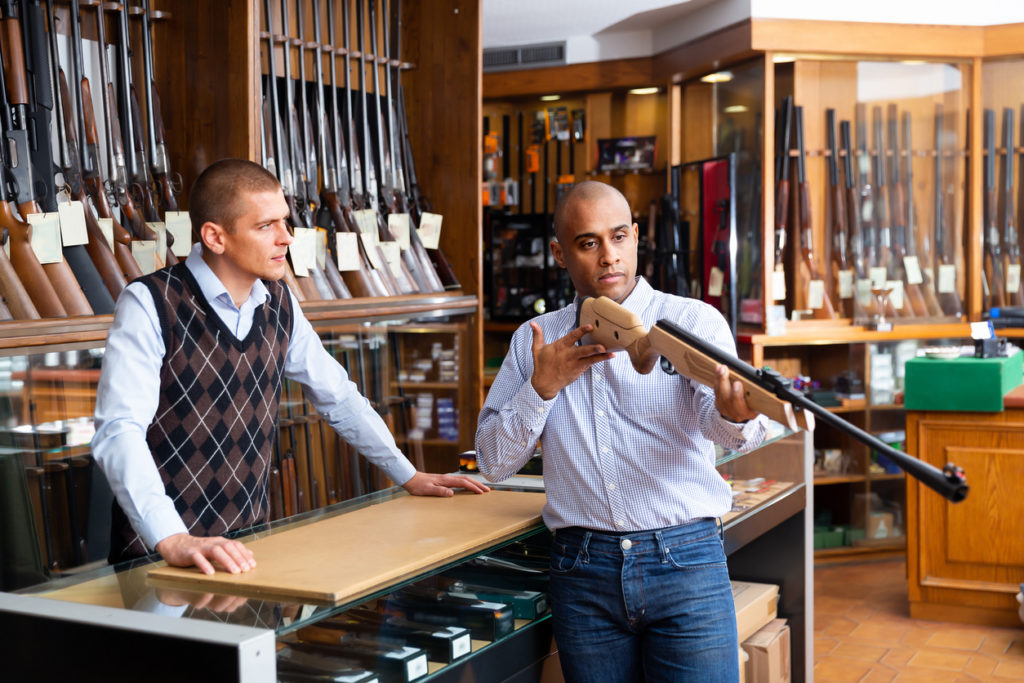 Hispanic man examining hunting rifle and consulting with salesman